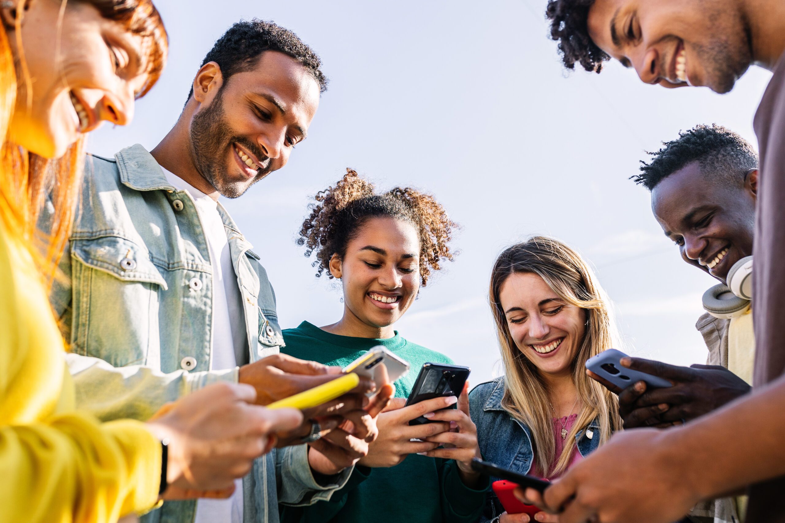 Young group of happy friends using smart mobile phone together outdoors